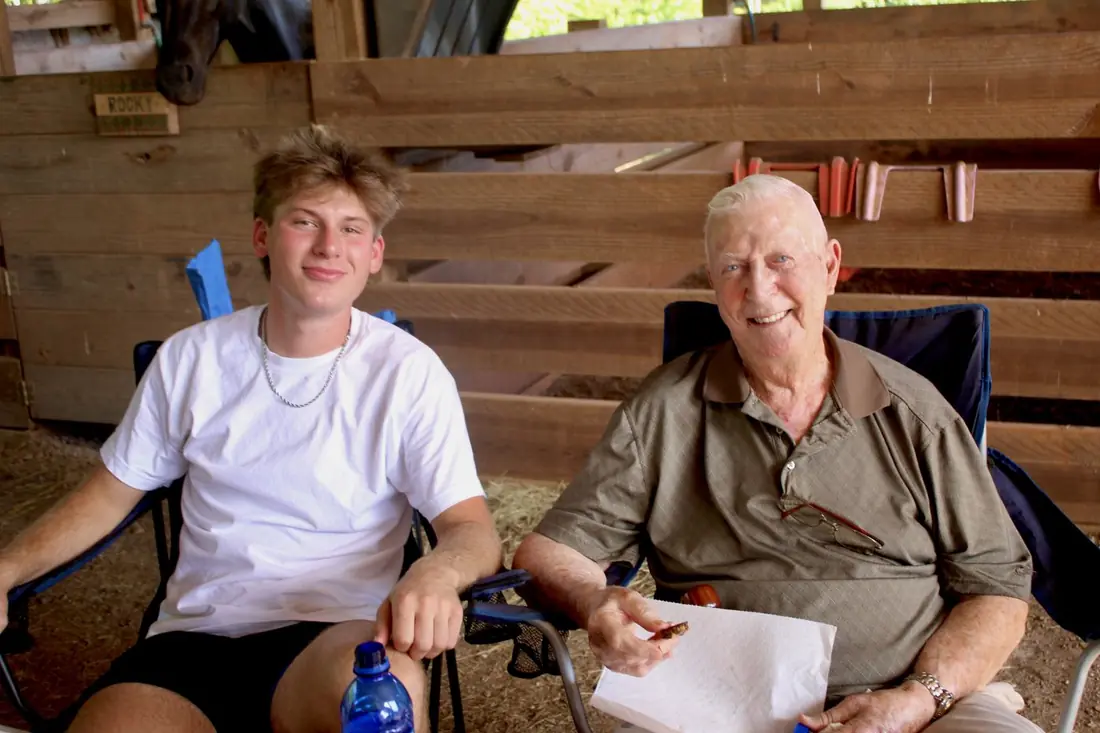 A young man and an older gentleman sitting side by side in the barn