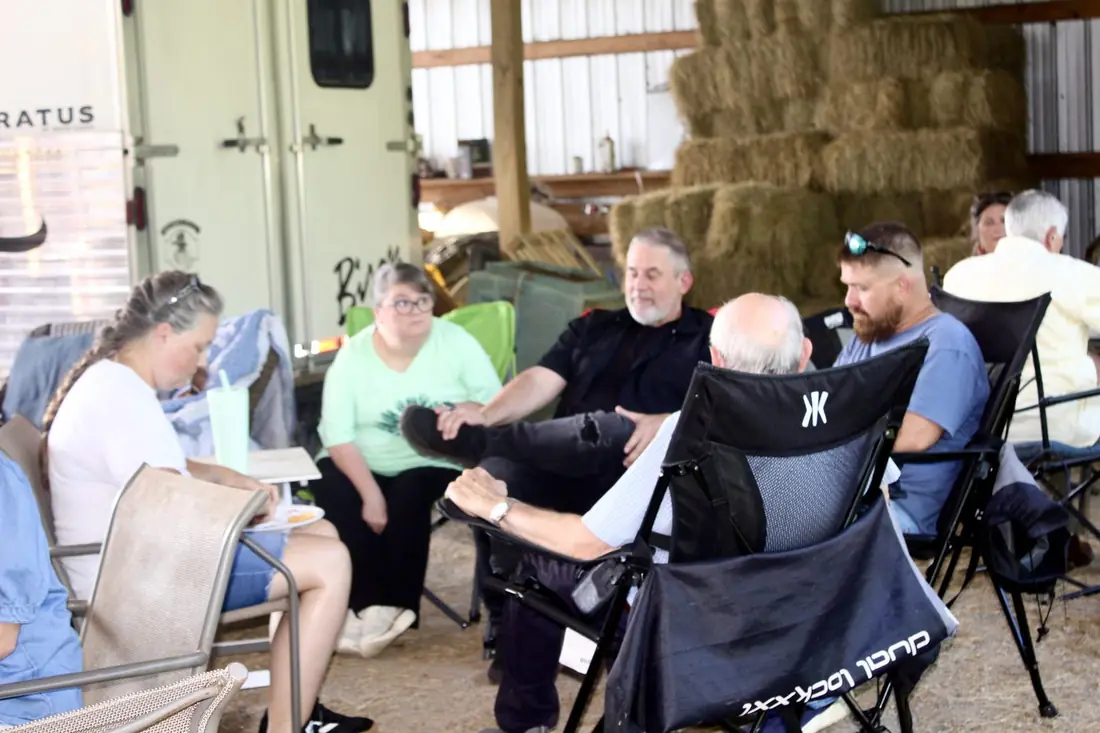 A circle of friends visiting in camp chairs inside the barn