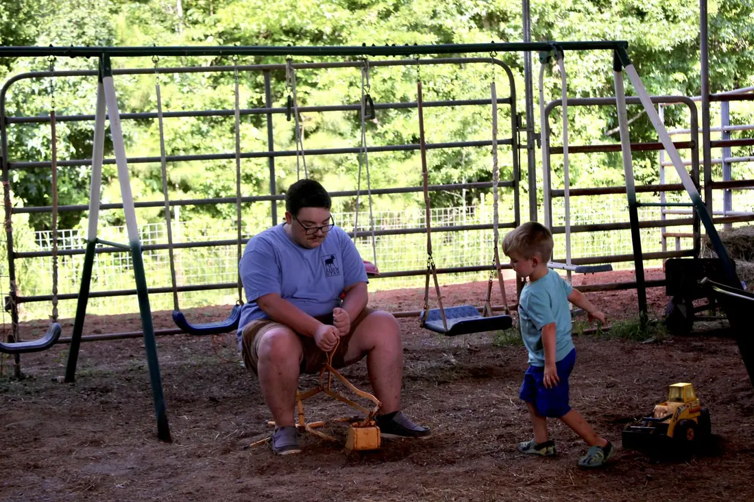 A young man on a swing beside a little boy with a toy truck
