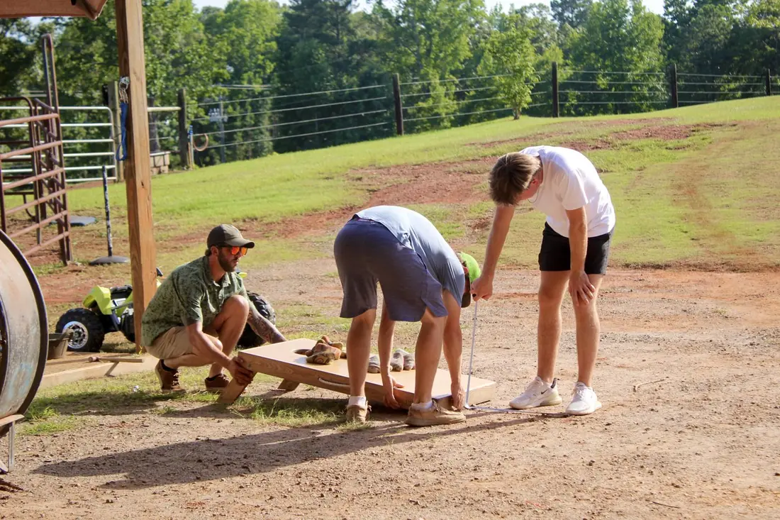 Three young men setting up a cornhole board on the lawn