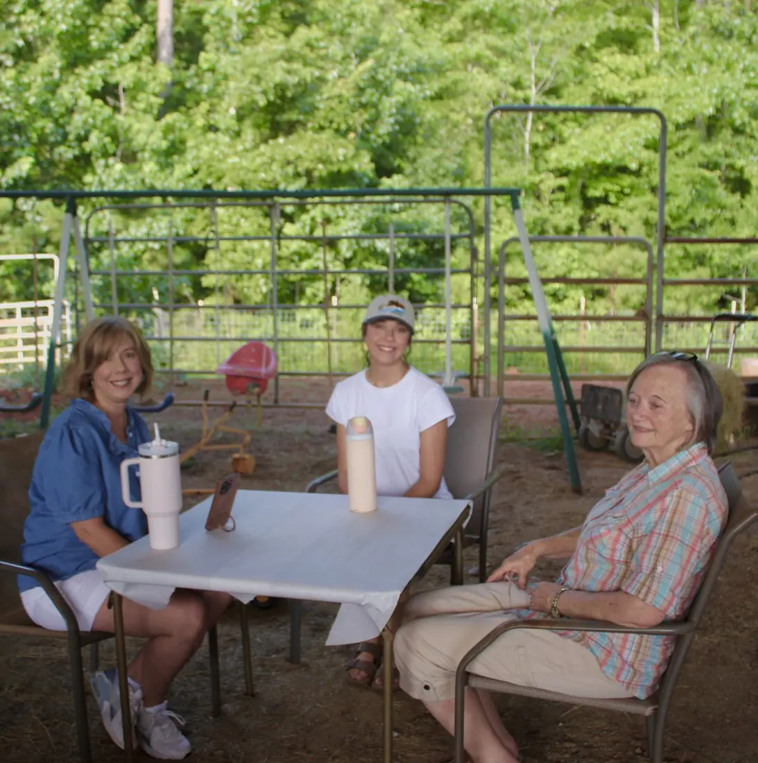 Three women smiling at an outdoor table by the swing set