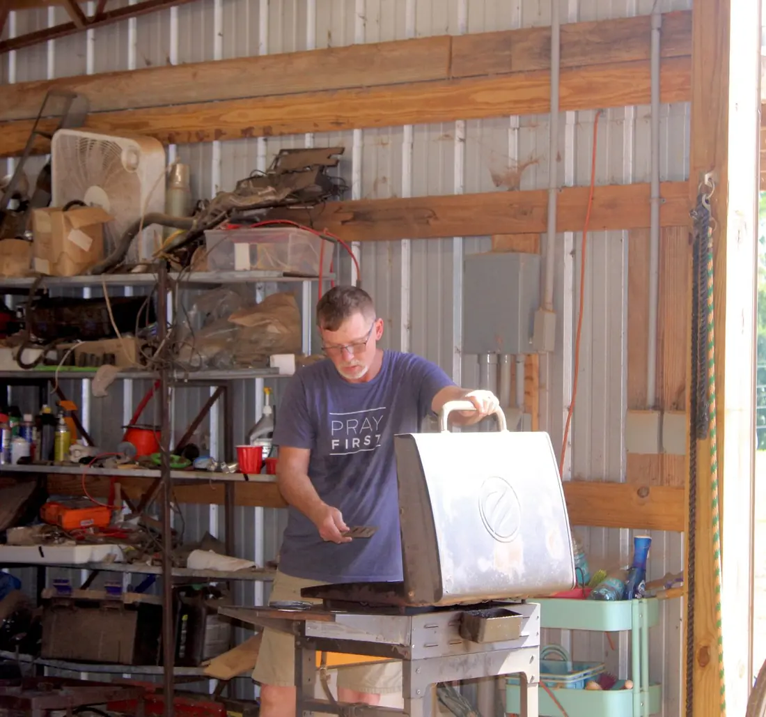 A man in a Pray First shirt tending the grill in the barn